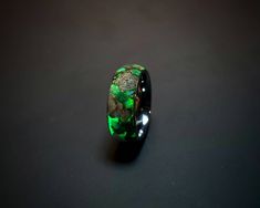 a ring with green and black stones in it on a dark surface, close up