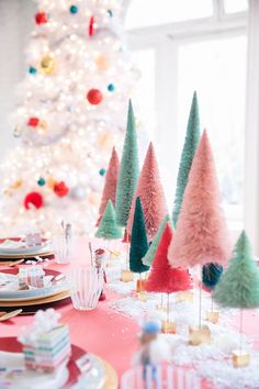 the table is set for christmas dinner with colorful trees on it and plates in front