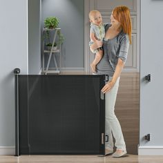 a woman holding a baby standing in front of a black screen with the door open