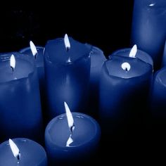 many blue candles are lit in the dark with one white candle sticking out of it's center