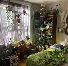 a bedroom filled with lots of plants next to a window covered in green blankets and pillows