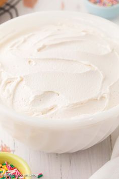 a bowl filled with white frosting next to sprinkles on a table