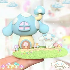 a hand holding a small blue mushroom house with two little white sheep in front of it