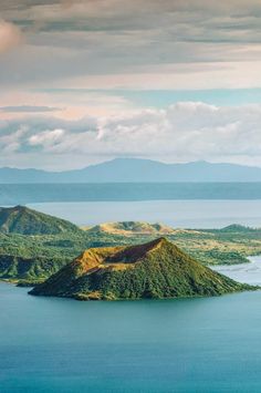 an island in the middle of water surrounded by land and mountains with clouds above it