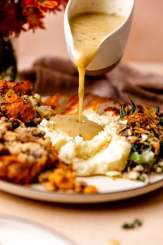 a person pouring sauce over a plate of food on a table with flowers in the background