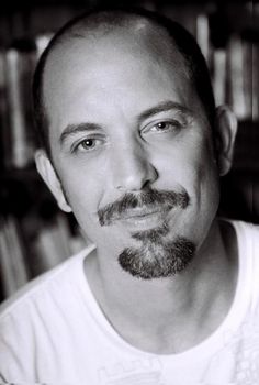 a black and white photo of a man with a beard in front of bookshelves