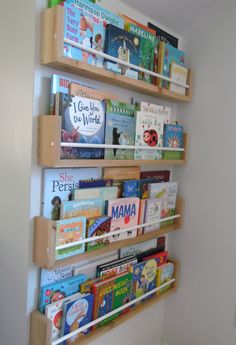 three wooden bookshelves holding children's books on the wall in a child's room