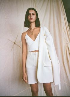 a woman standing in front of a backdrop wearing a white suit and matching necklaces