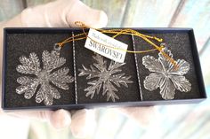 a person holding three snowflakes in a black gift box with gold string