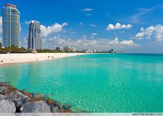 people are swimming in the clear blue water at an ocean beach with high rise buildings