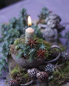 a candle is lit in a bowl filled with plants and pine cones