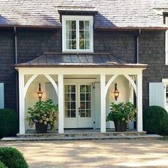 a house with white trim and two large potted plants on the front porch area