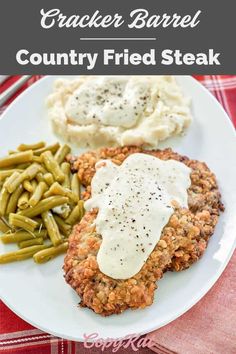 a white plate topped with meat covered in gravy next to green beans and mashed potatoes