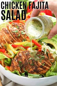 someone pouring dressing onto a salad in a white bowl with lettuce and red peppers