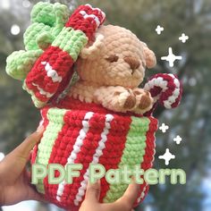 a hand holding a small crocheted teddy bear in a striped cup with candy canes