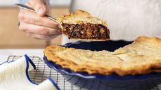 a person holding a piece of pie in front of a pie dish on a cooling rack