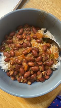 a blue bowl filled with rice and beans on top of a wooden table next to a spoon