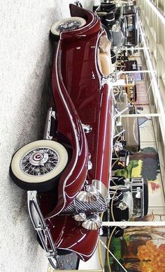 an old red car is parked in front of a wall full of other antique cars