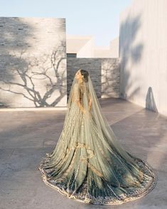 a woman in a green and gold bridal gown standing on the ground with her back to the camera