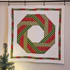 a green and red christmas tree skirt hanging on the wall next to a small fir tree