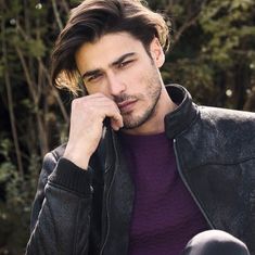 a young man in a leather jacket is posing for a photo with his hand on his chin