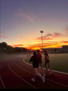 three people running on a track at sunset