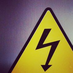 a yellow and black sign with a lightning bolt on it's back side in front of a gray wall