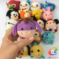 a hand holding a small crocheted doll surrounded by many other stuffed animal toys