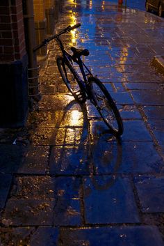 a bicycle parked on the side of a wet street in the rain with its lights on