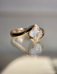 a gold ring with a princess cut diamond in the center on a reflective surface,