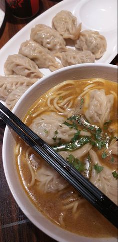 some dumplings and noodles are in a white bowl with chopsticks on the side