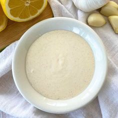 a white bowl filled with sauce next to sliced lemons and garlic