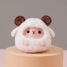 a small stuffed sheep sitting on top of a wooden stand with its eyes wide open