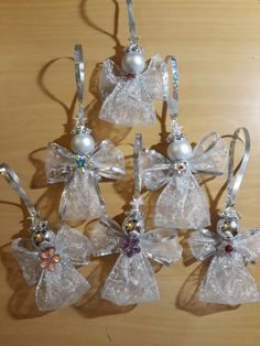 six glass angel ornaments with bows and pearls hanging from strings on a wooden table top