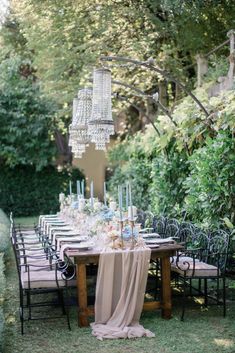 an outdoor dining table with chandelier hanging from the ceiling, surrounded by greenery