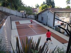 two men playing basketball on an outdoor court in the backyard with trees and shrubs surrounding them