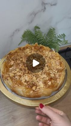 a person is holding a pie on a gold plate and pointing to it with their finger