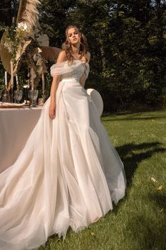 a woman in a wedding dress standing next to a table with flowers and feathers on it