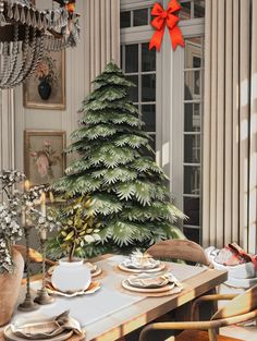 a christmas tree sitting next to a dining room table with plates and cups on it