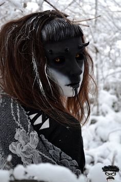 a woman with black makeup and white face paint in the snow, wearing a wolf mask