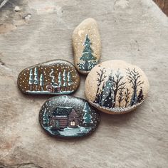 three painted rocks sitting on top of a rock covered in snow next to a forest