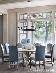 a dining room table with blue chairs and chandelier in front of large windows