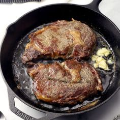 two steaks cooking in a skillet on top of a stove with butter and seasoning