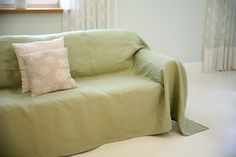 a green couch sitting in front of a window with two pillows on it's back