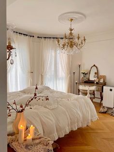 a bedroom with white bedding and chandelier hanging from the ceiling next to a window