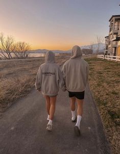 two people walking down a road with their back to the camera, both wearing jackets and shorts