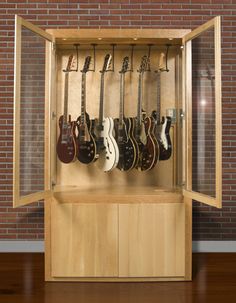 a display case with guitars in it on the floor next to a brick wall and wooden floors