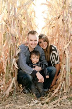 a man and woman pose for a photo with their son in the middle of a corn field