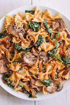 a white bowl filled with pasta and spinach on top of a wooden table next to a fork