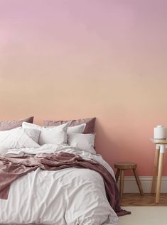 a bedroom with pink walls and white linens on the bed, along with a wooden side table